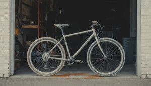 Photographie réaliste d’un vélo de ville ou VTT dans un garage, avec la chaîne et les écrous du cadre couverts de résidus blancs de sel et des traces de rouille naissante, un chiffon microfibre et un spray lubrifiant en arrière-plan.